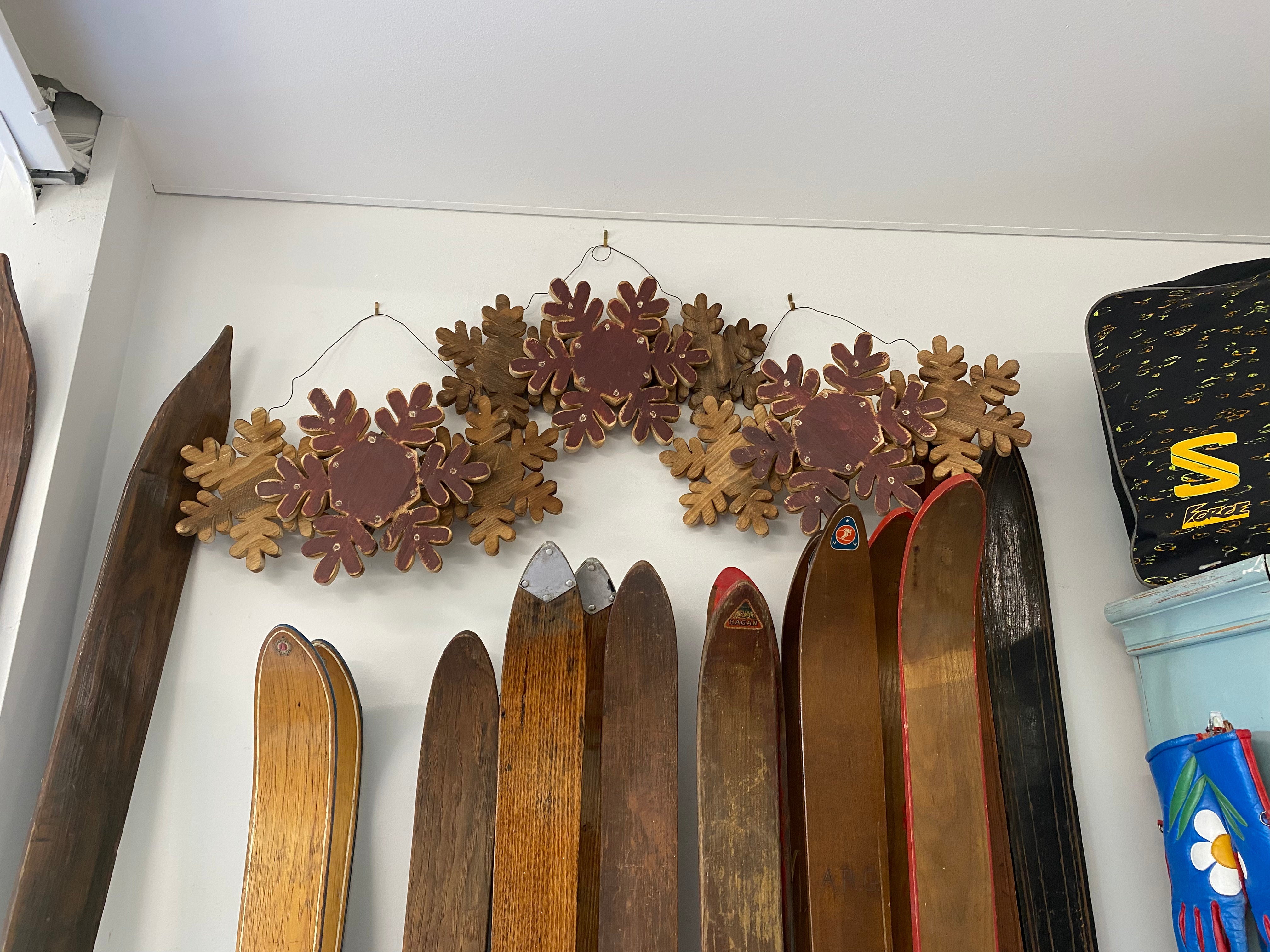 3 Wood snowflake wall decor with Led lights shown as the lights are dimming, on a white wall with 3 HAM Rabbit Prints & wooden skis underneath the snowflakes