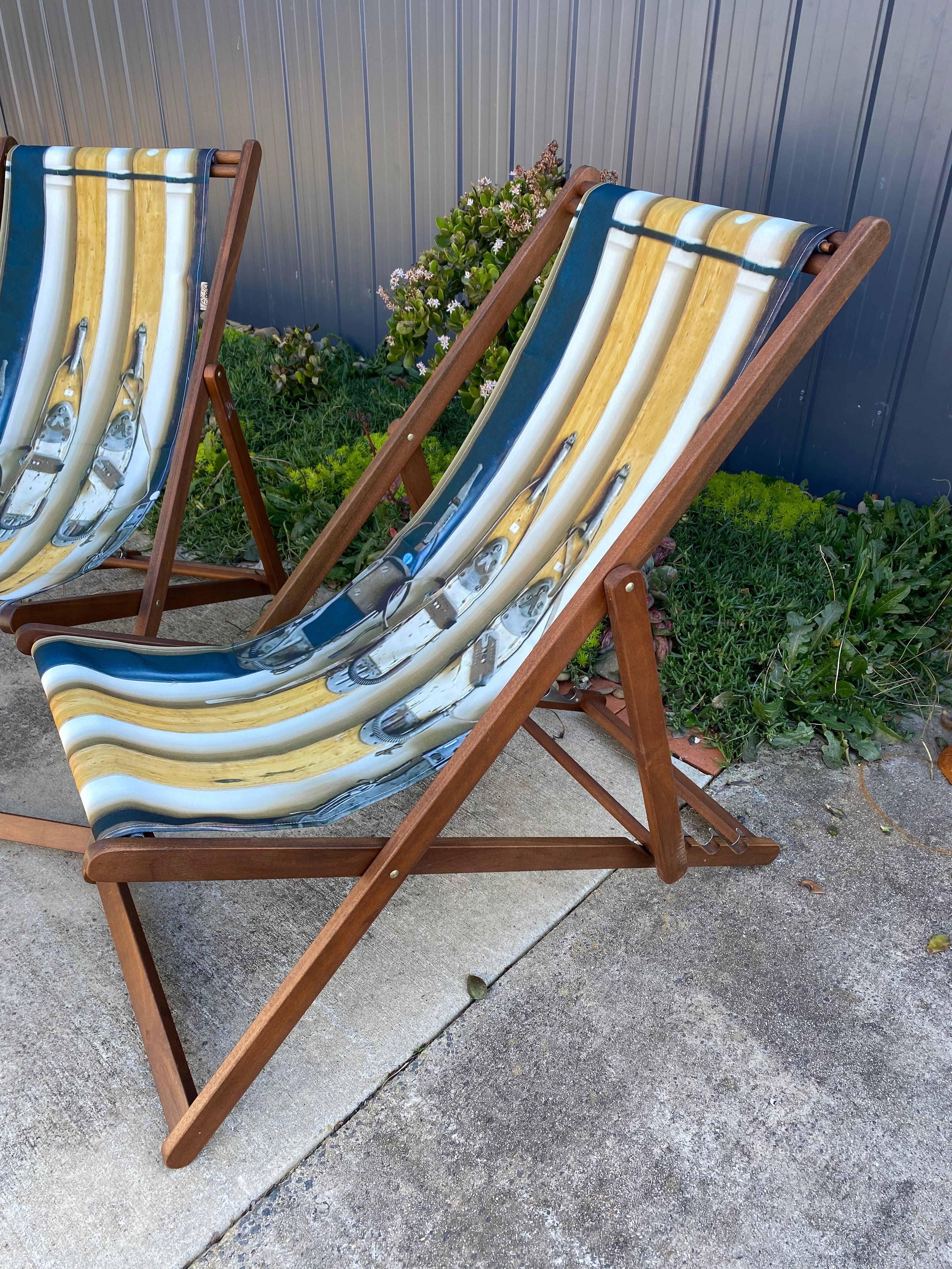 Side View. Pair of Coast & Valley Deck Chairs: Vintage Ski design showing 2 pairs of vintage wooden skis with bindings. On a concrete floor against a blue steel shed and door with garden bed in the background Edit alt text