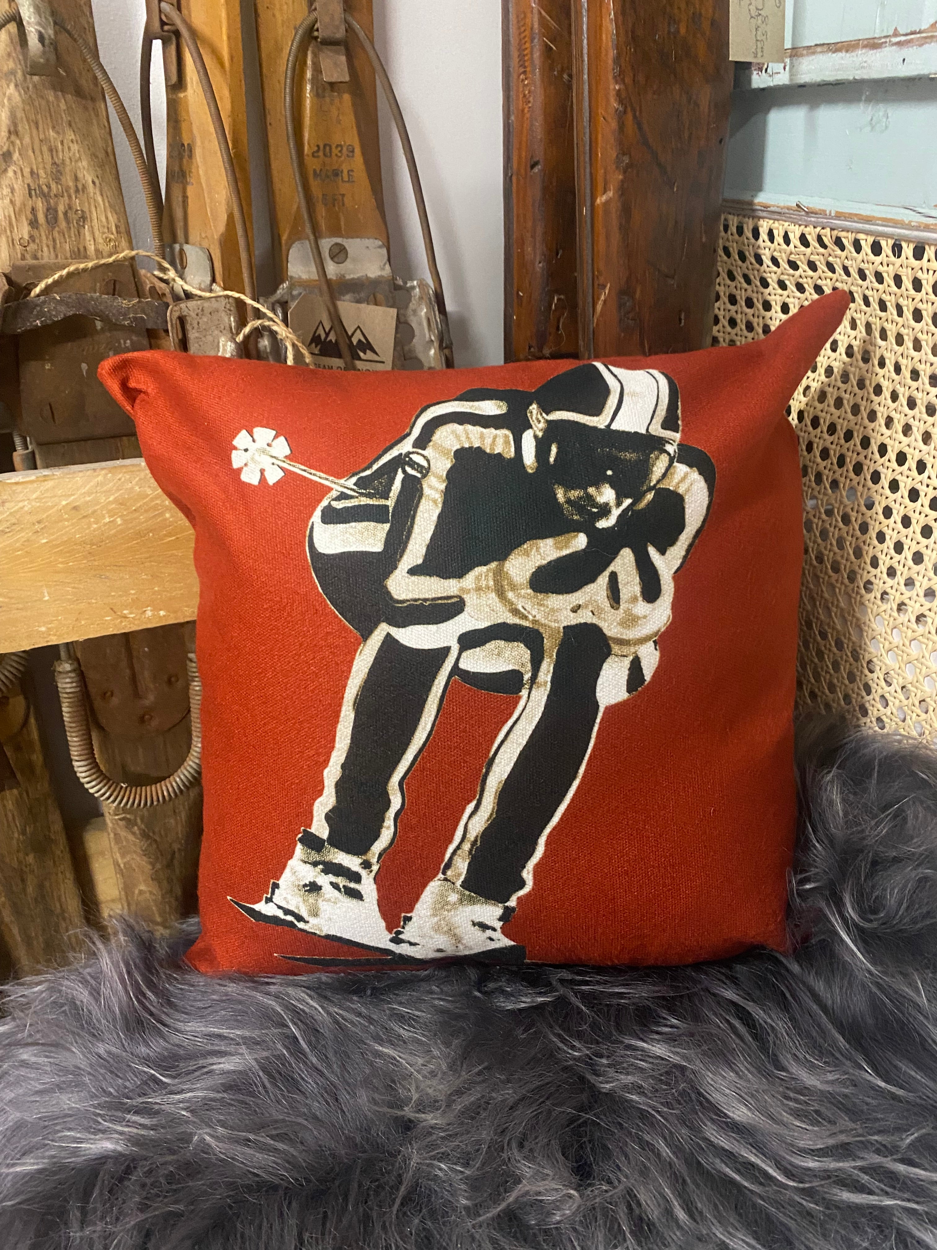 vintage ski racer graphic on red coloured cushion, on a white sheepskin against vintage wooden skis and a blue dresser