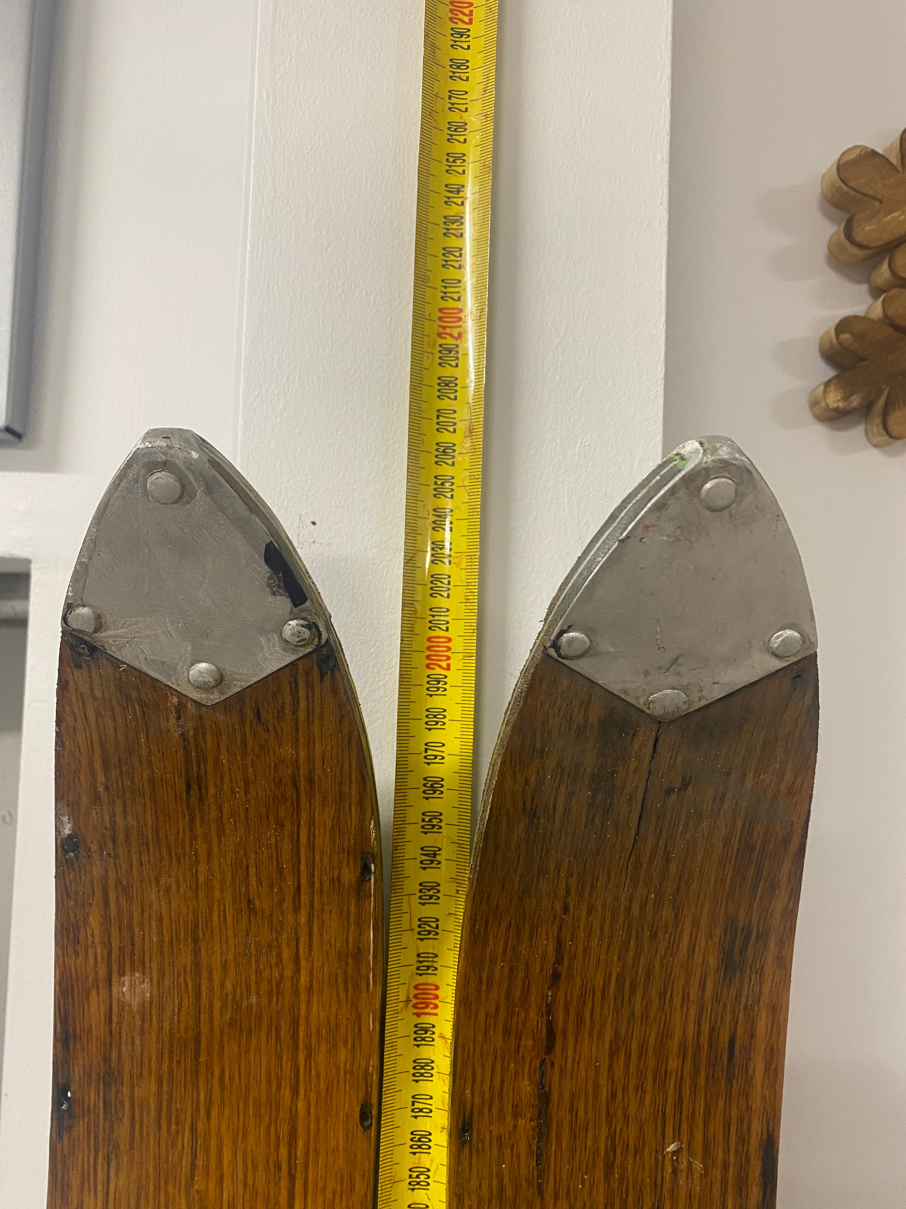 Ski Tips Front View: Vintage Wooden Skis with metal bindings. Lent against a white wall, with a tape measure on the wall.