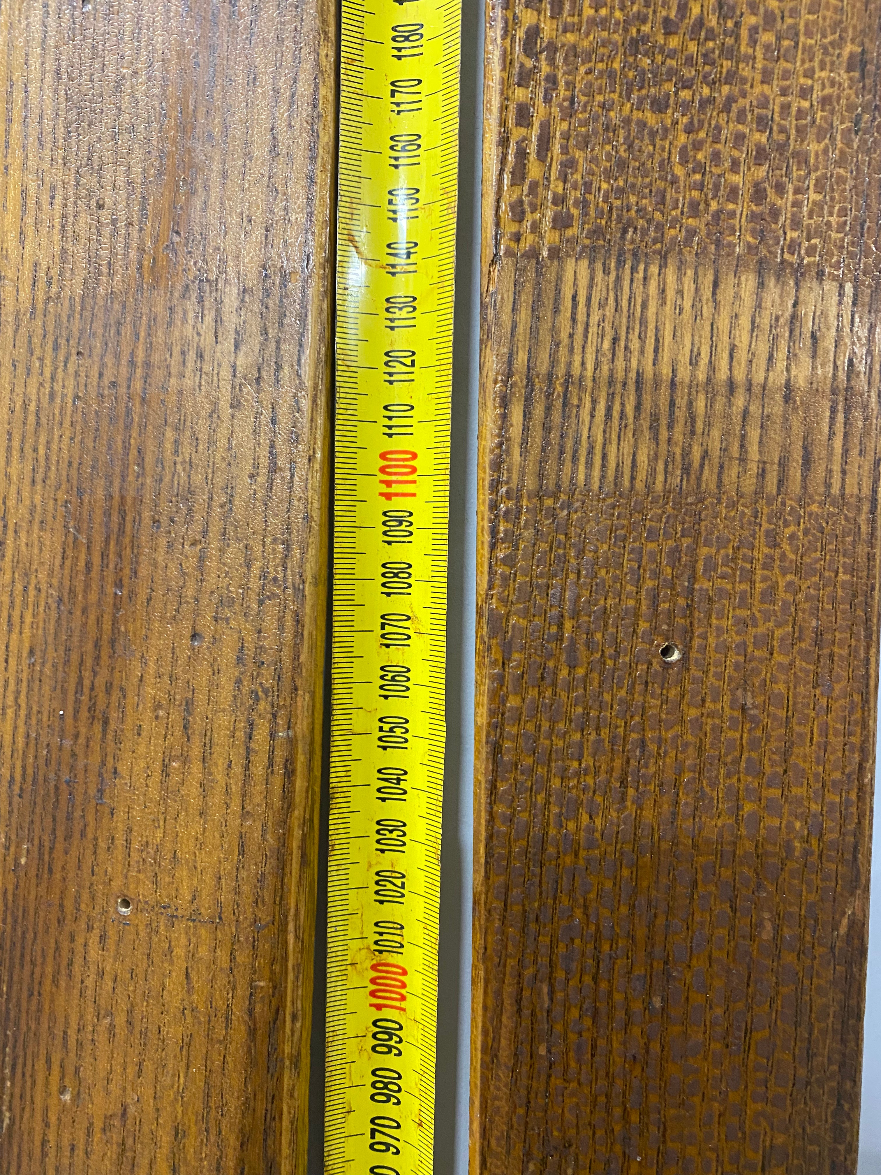 Close up of middle of skis. Unbranded vintage wooden skis, showing small drilled holes. leaning against white painted wall with yellow measuring tape.