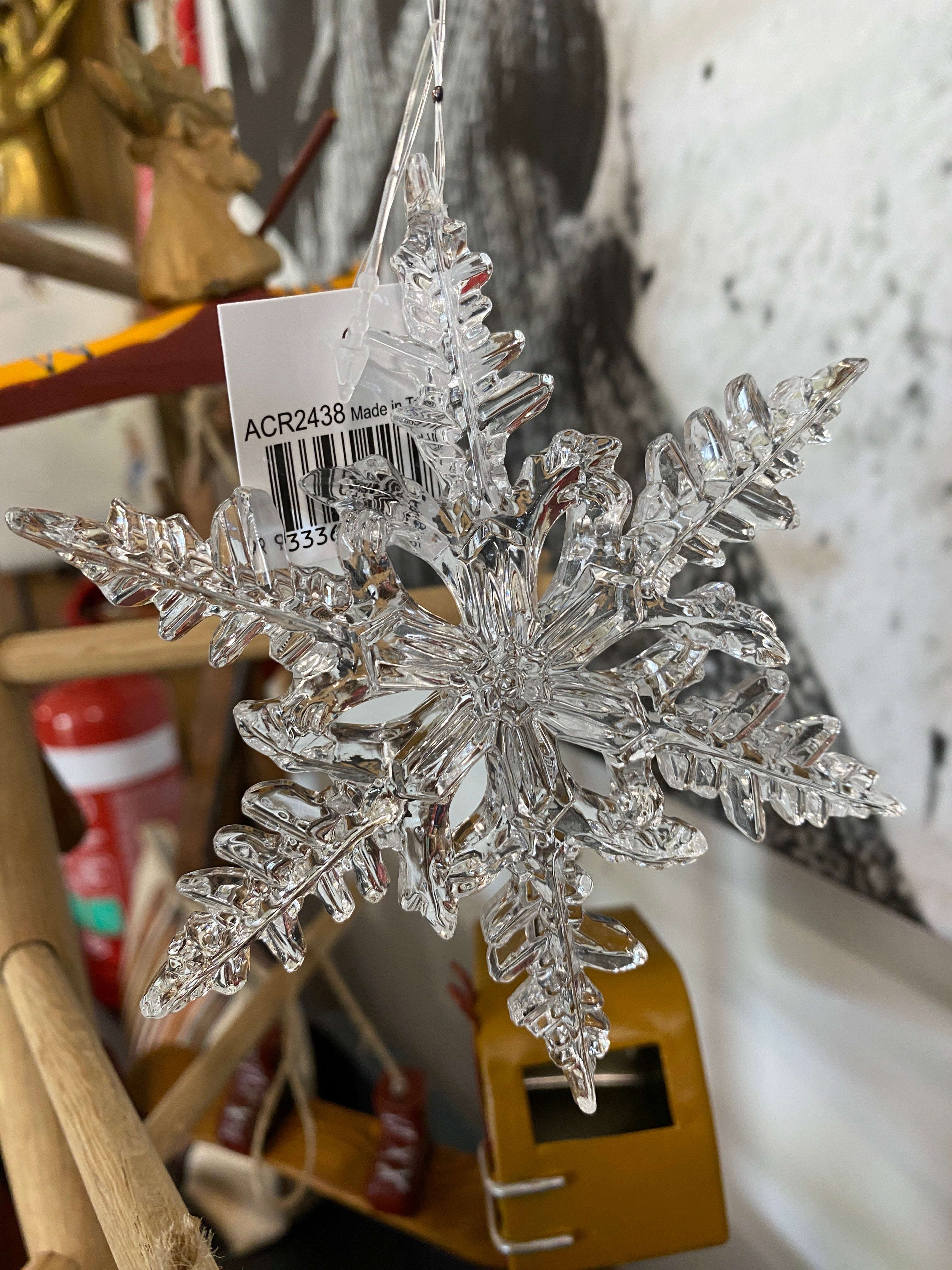 Close up of Clear acrylic snowflake hanging ornament in front of a black and white photo and hanging on a wooden frame with other hanging snow themed ornaments