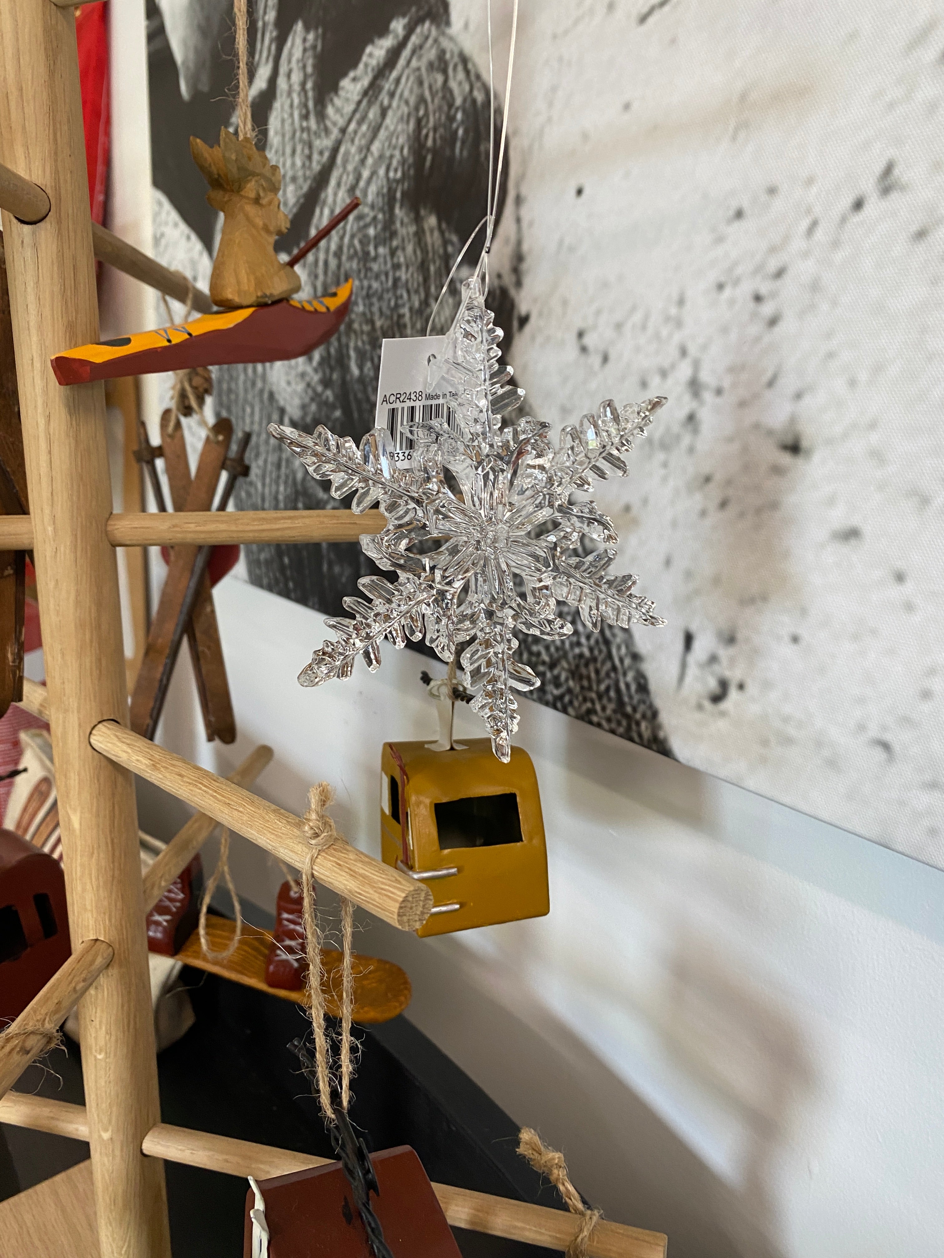 Clear acrylic snowflake hanging ornament in front of a black and white photo and hanging on a wooden frame with other hanging snow themed ornaments