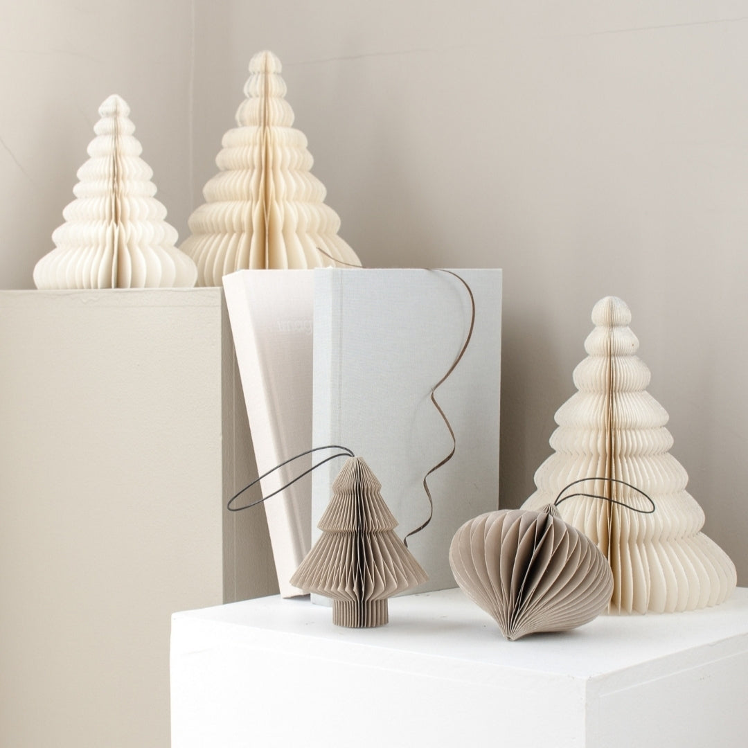 Selection of 3 Off-white Paper Standing Trees, and two hanging paper ornaments in a tree shape and bauble shape in mushroom colour, all sitting on a number of white and mushroom colour painted boxes