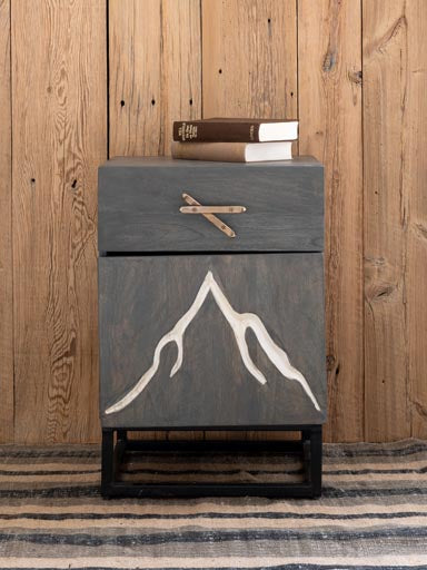 Front view of Bedside table engraved with a mountain & ski handle with a wood panelled wall in the background and a rug on the floor