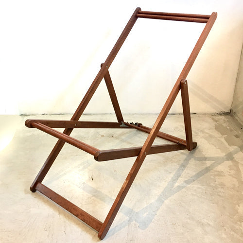 Deck chair frame without fabric sling, on concrete floor against white walls