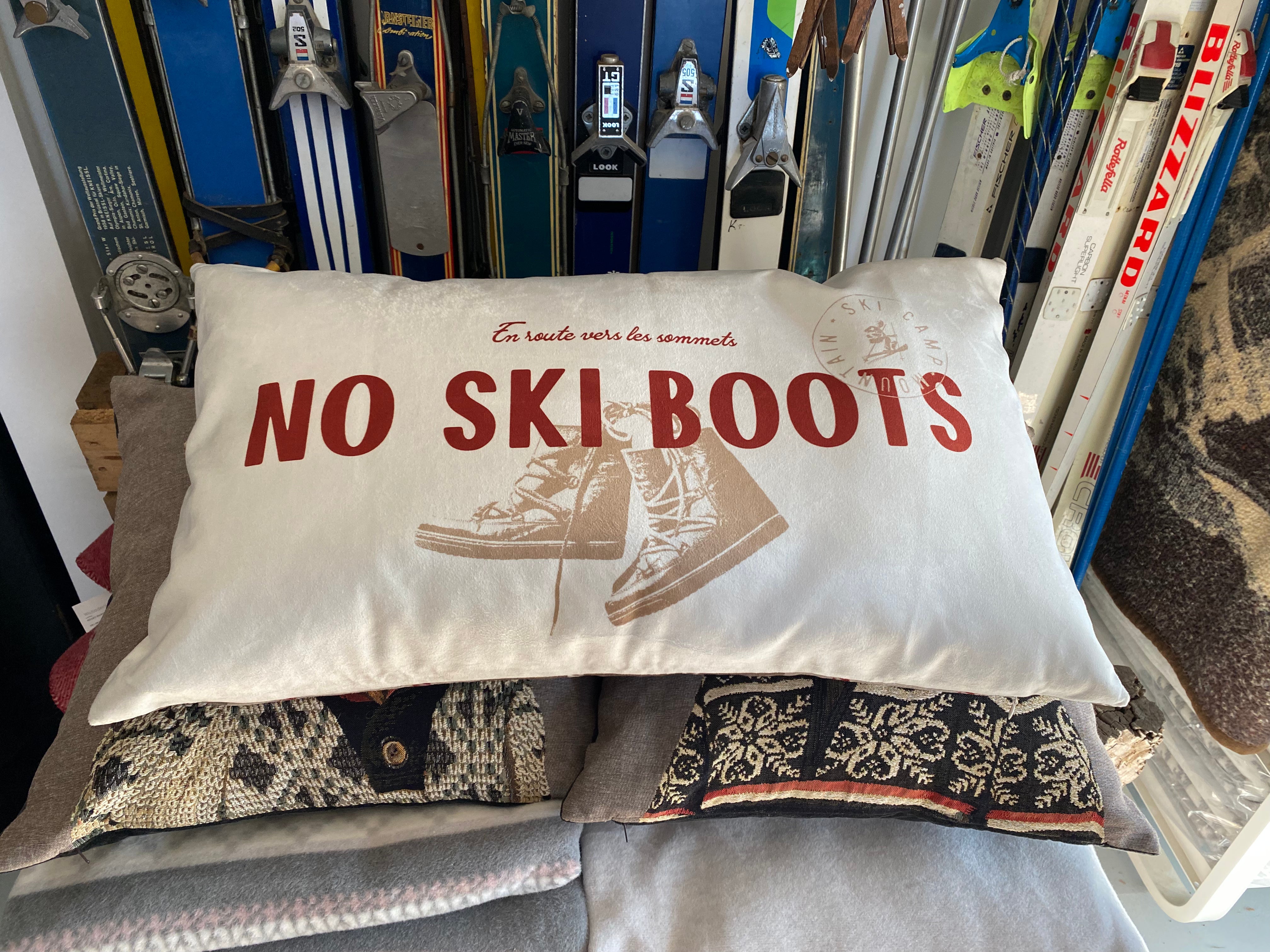 No Ski Boots Cushions sitting on top of other cushions and leaning against a backdrop of old skis