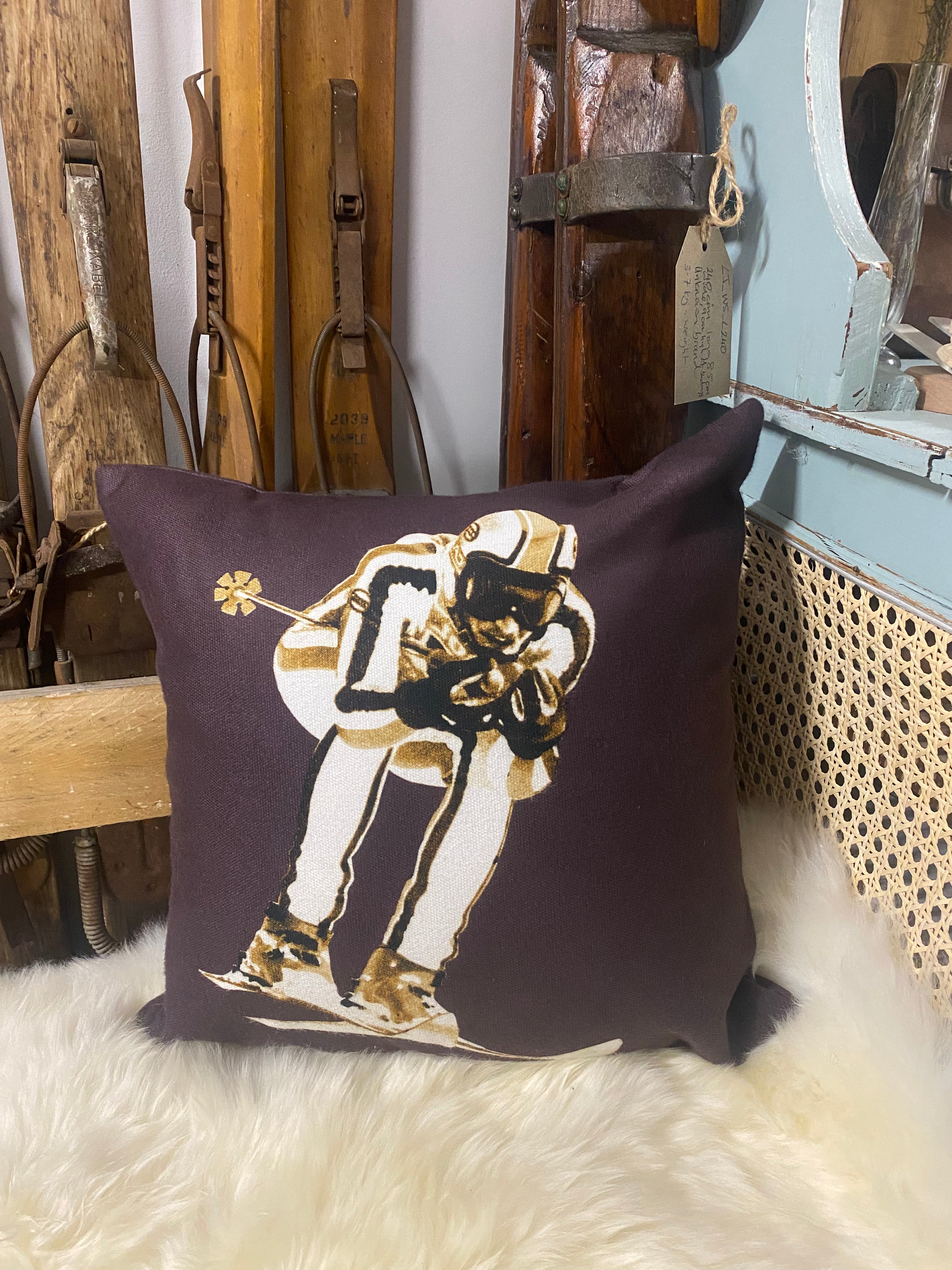 vintage ski racer graphic in white & beige on chocolate coloured cushion, on a white sheepskin against vintage wooden skis and a blue dresser