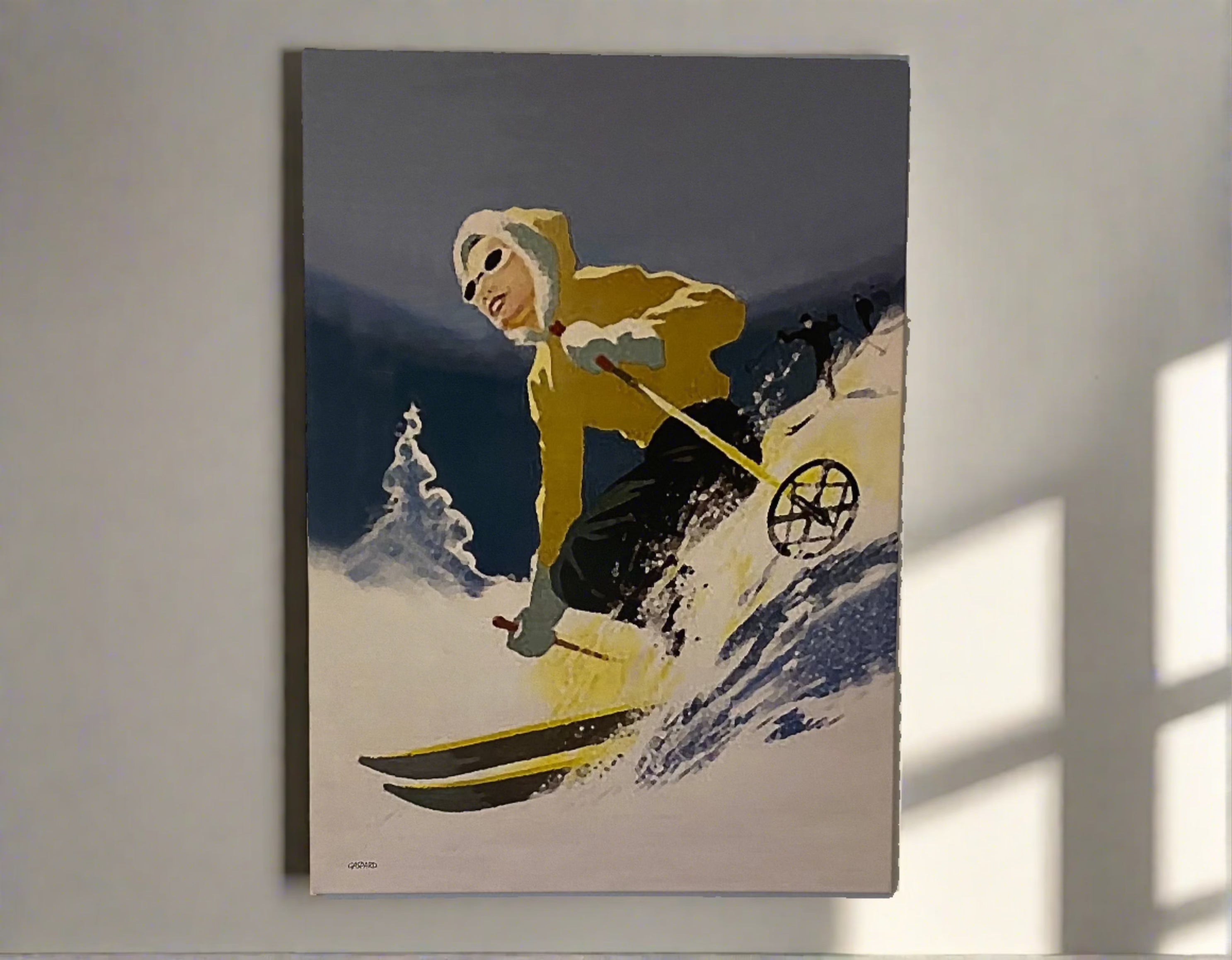 Canvas depicting a woman in a yellow jacket with a white fur at the edge of the hood and blue pants skiing downhill, leaning to the right into the hill with a tree and the shadow of the mountains in the background below a blue sky.  Hanging on a white wall