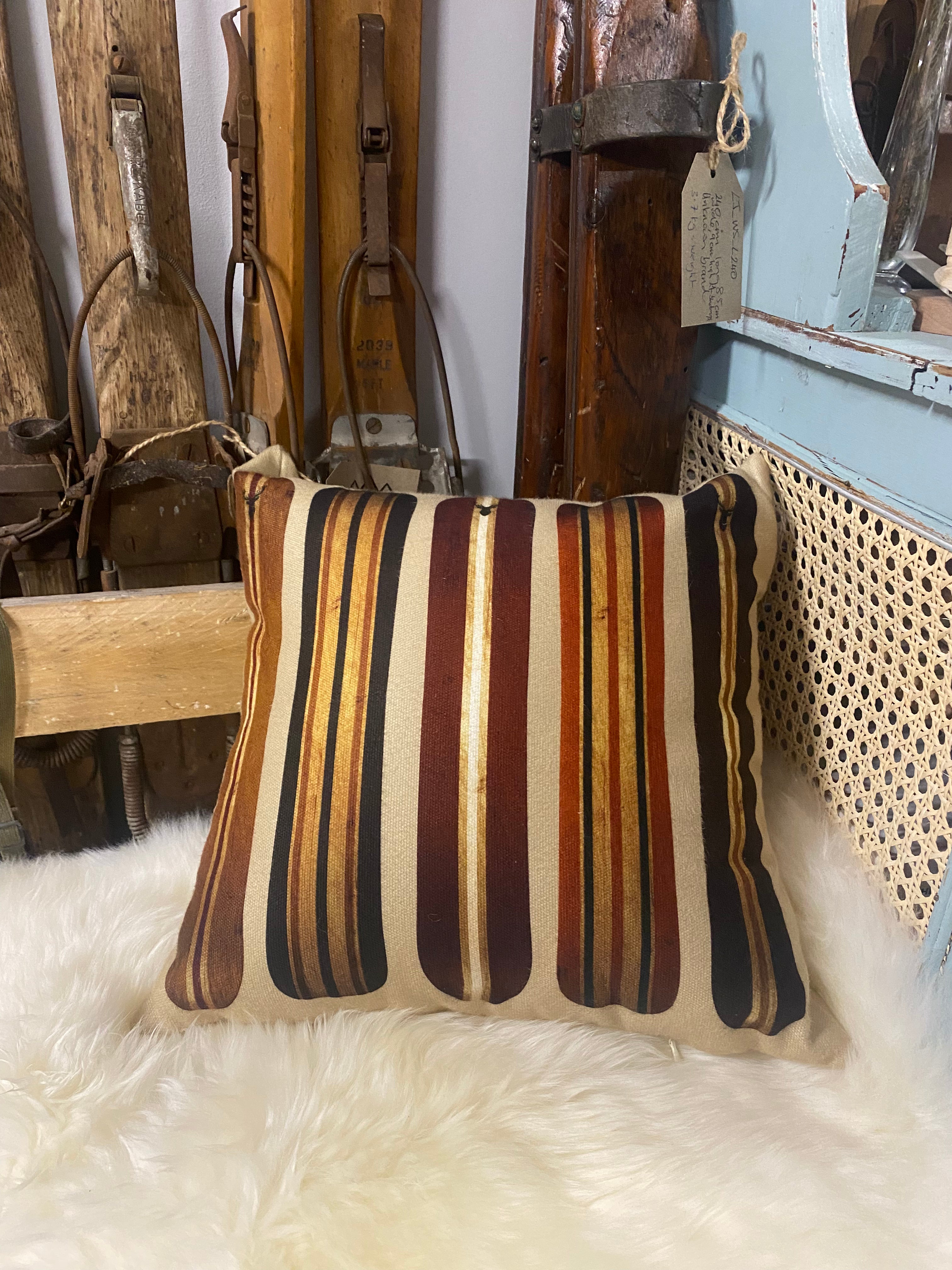 Vintage Style Snowboard Cushion: photo of wooden style striped snowboards on a beige cushion Cushion resting on a white sheepskin, against wooden skis and a blue cupboard