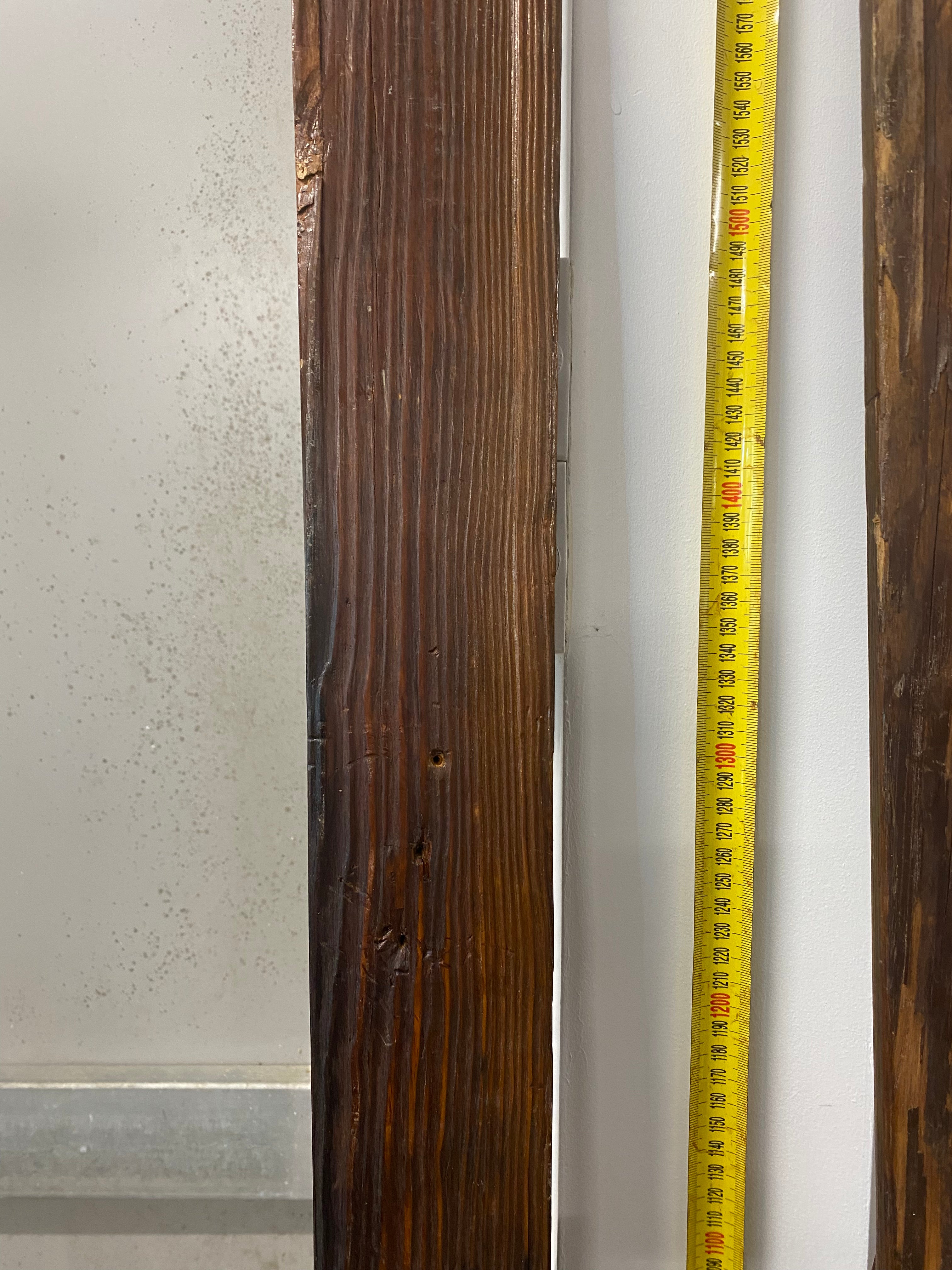 Vintage Wooden Skis: close up of bases of both skis on white wall and resting against a yellow measuring tape.