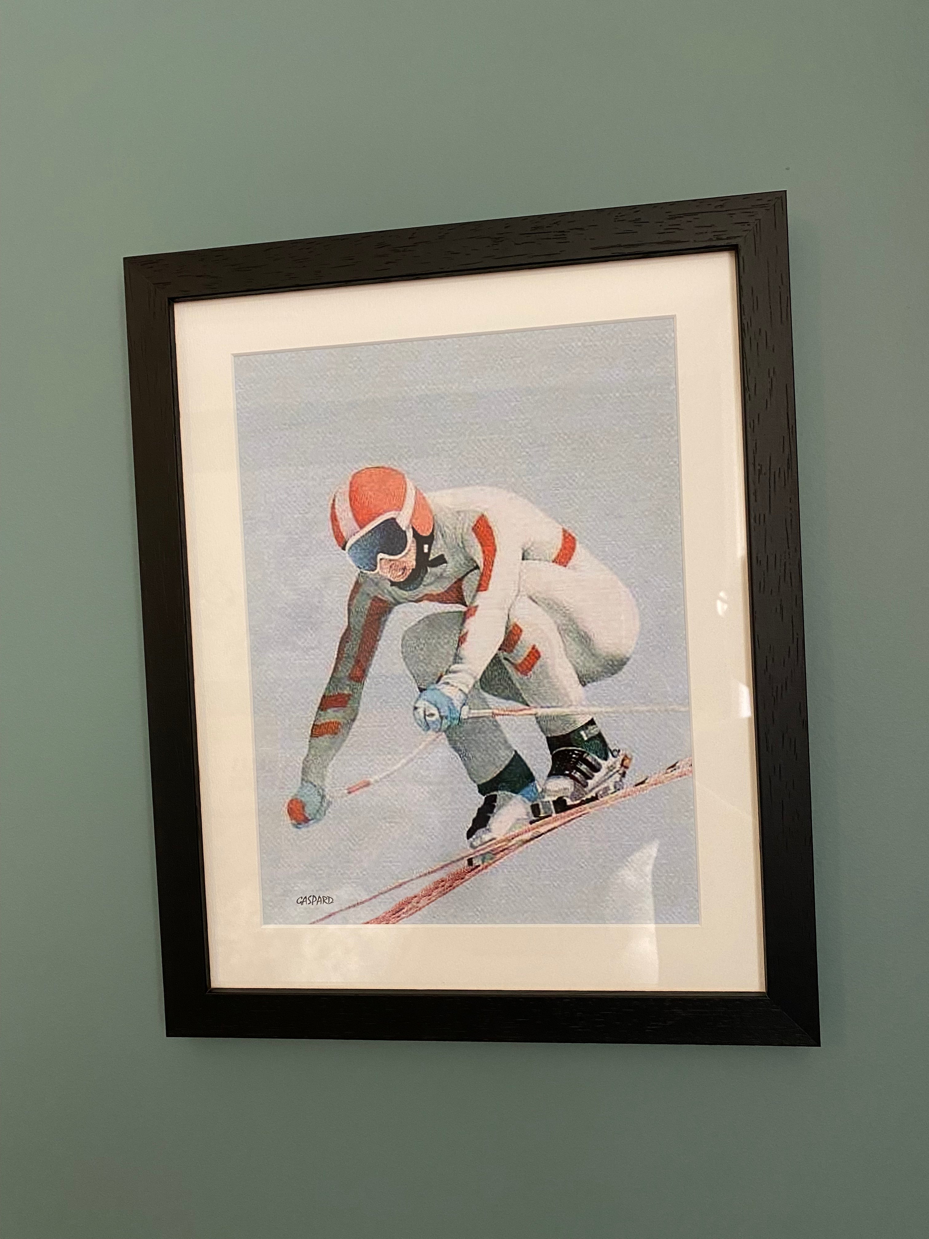 Black framed print of a person in a white fitted racing suit with red stripes, a red helmet with a central white stripe, with skis, boots and poles in a crouched position airborne and skiing downhill, with a light blue sky in the background, hanging on a green wall. 