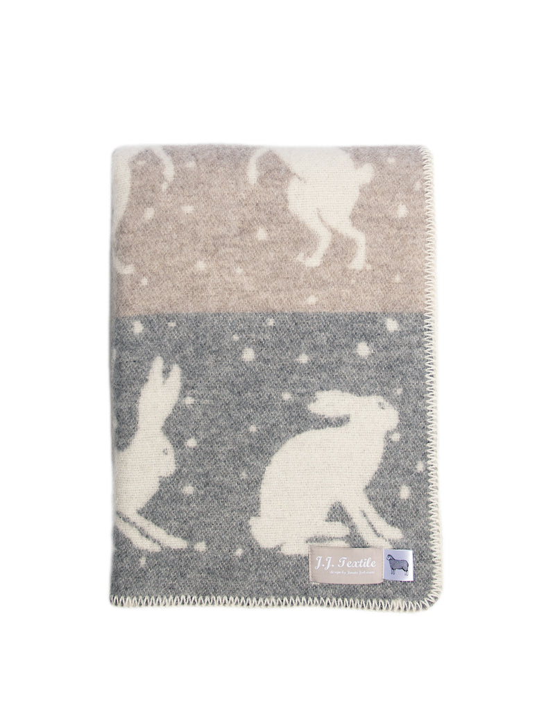 Boxing hares, sparring against a snowy background. The wintery scene on this pure wool stitched blanket will make you want to snuggle up under its soft grey and soft brown design and dream of Christmas and long walks in the countryside.  Folded blanket showing a corner of the blanket